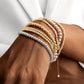 Mehrere Armbänder aus 18 Karat Gold und Weißgold in Kugeldesign, elegant am Handgelenk getragen und kunstvoll übereinander gestapelt – moderner, luxuriöser Look in Kombination mit weißem Outfit.