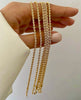 Nahaufnahme mehrerer Armbänder aus 18k Gelbgold in gedrehter Kordeloptik, die locker über die Finger einer Hand gelegt sind. Die polierten, spiralförmig verflochtenen Glieder reflektieren das Licht und erzeugen einen intensiven Goldglanz. Hintergrund neutral und hell, Hand in weißem Stoffärmel.