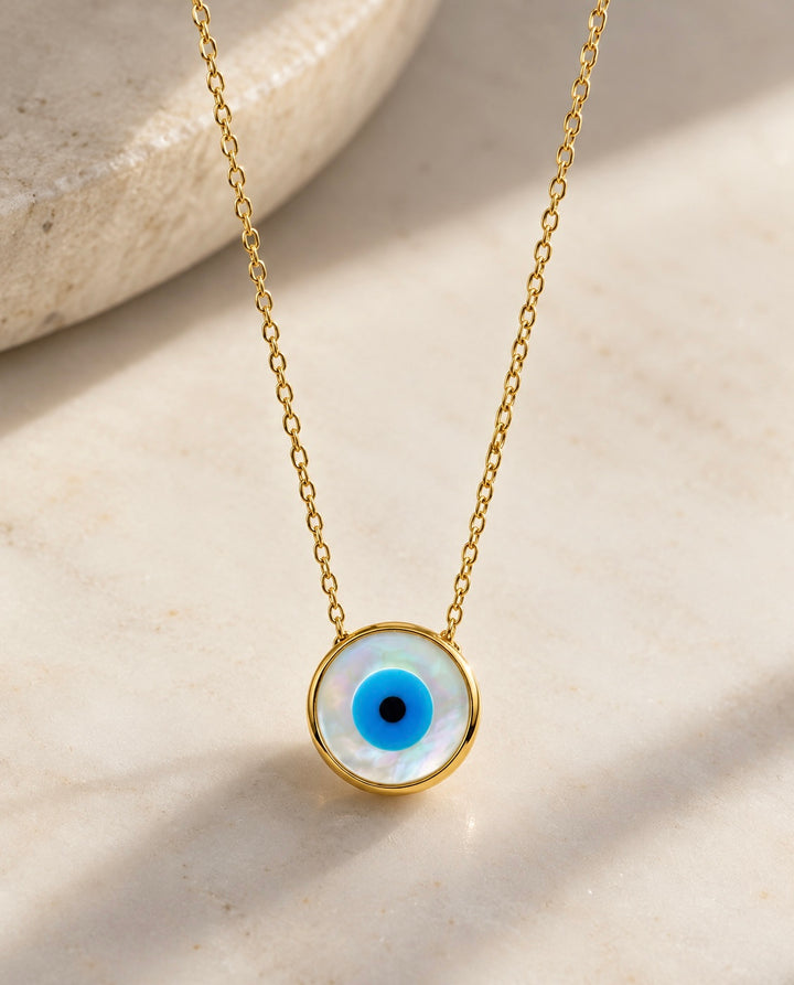 18 Karat Gold Halskette mit rundem Nazar-Anhänger aus schimmerndem Perlmutt und blauem Auge – filigraner Goldschmuck auf hellem Naturstein.