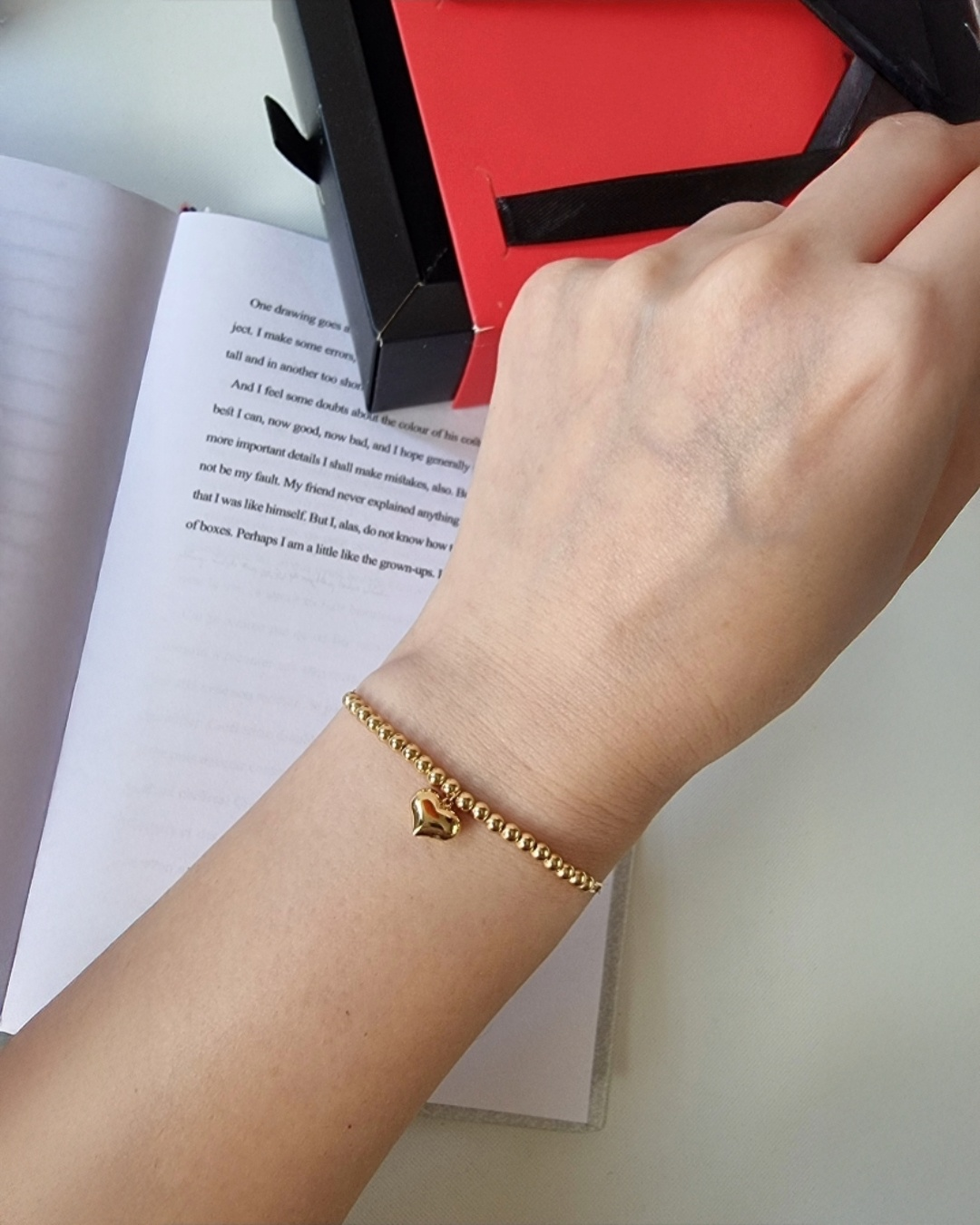 18k Gelbgold-Armband mit feiner Goldkugelkette und Herz-Anhänger, getragen am Handgelenk, elegante Nahaufnahme auf hellem Hintergrund.