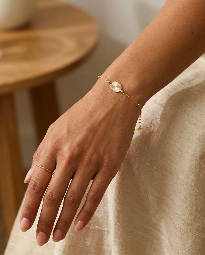 Filigranes Damenarmband aus 18 Karat Gelbgold mit rundem, strukturiertem Goldanhänger und feinen Goldkügelchen am Handgelenk.