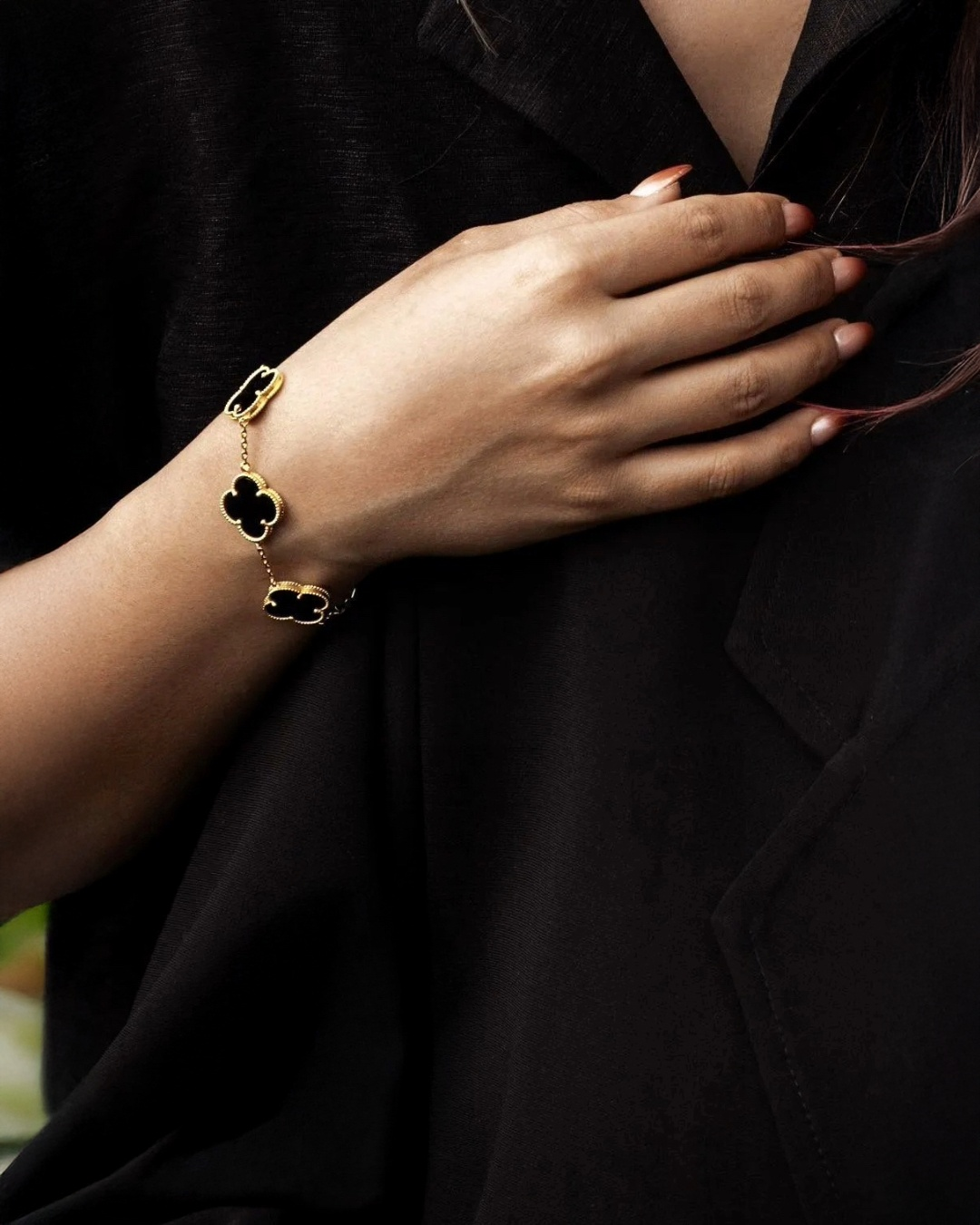 Handgelenk mit elegantem Armband aus 18k Gelbgold mit schwarzen, kleeblattförmigen Elementen, stilvoll getragen vor dunklem Stoffhintergrund.