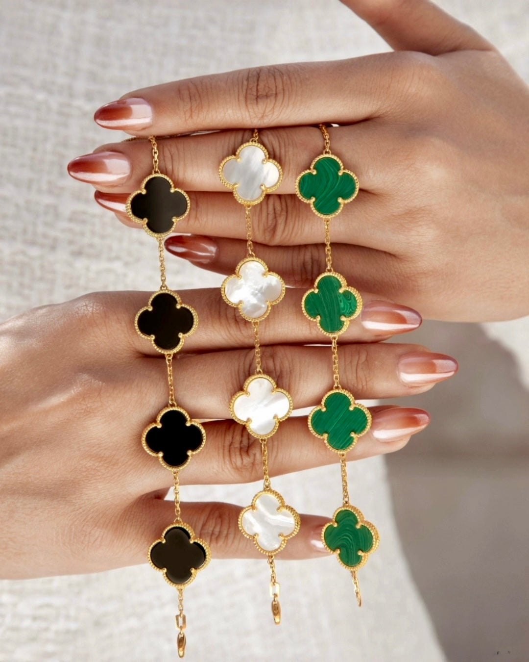 Feine Armbänder aus Gelbgold 18k mit filigranen Kleeblatt-Elementen, präsentiert an den Händen getragen; Varianten mit schwarzer Onyx-Optik, weißem Perlmutt und grünem Malachit, elegant kombiniert und detailreich in hochwertiger Verarbeitung dargestellt.