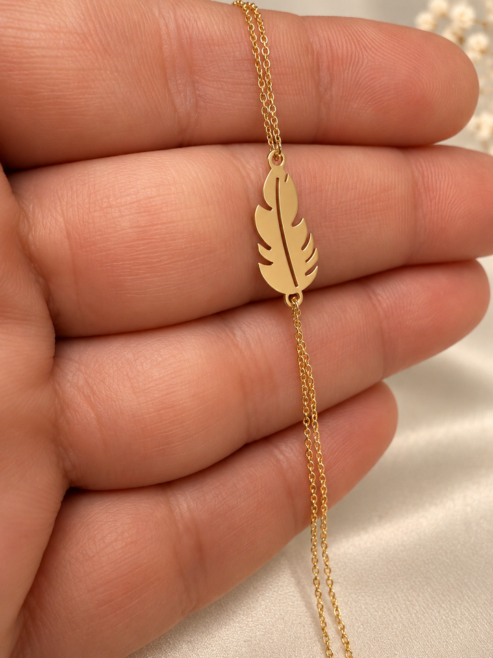 Nahaufnahme des goldenen Federmotivs am Armband Par aus 18 Karat Gelbgold mit zwei feinen Kettensträngen.