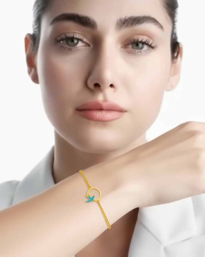 Armband aus 18k Gelbgold mit emaillierter Schwalbe im Kreis – getragen von einem Model mit weissem Blazer, elegant &amp; handgefertigt.