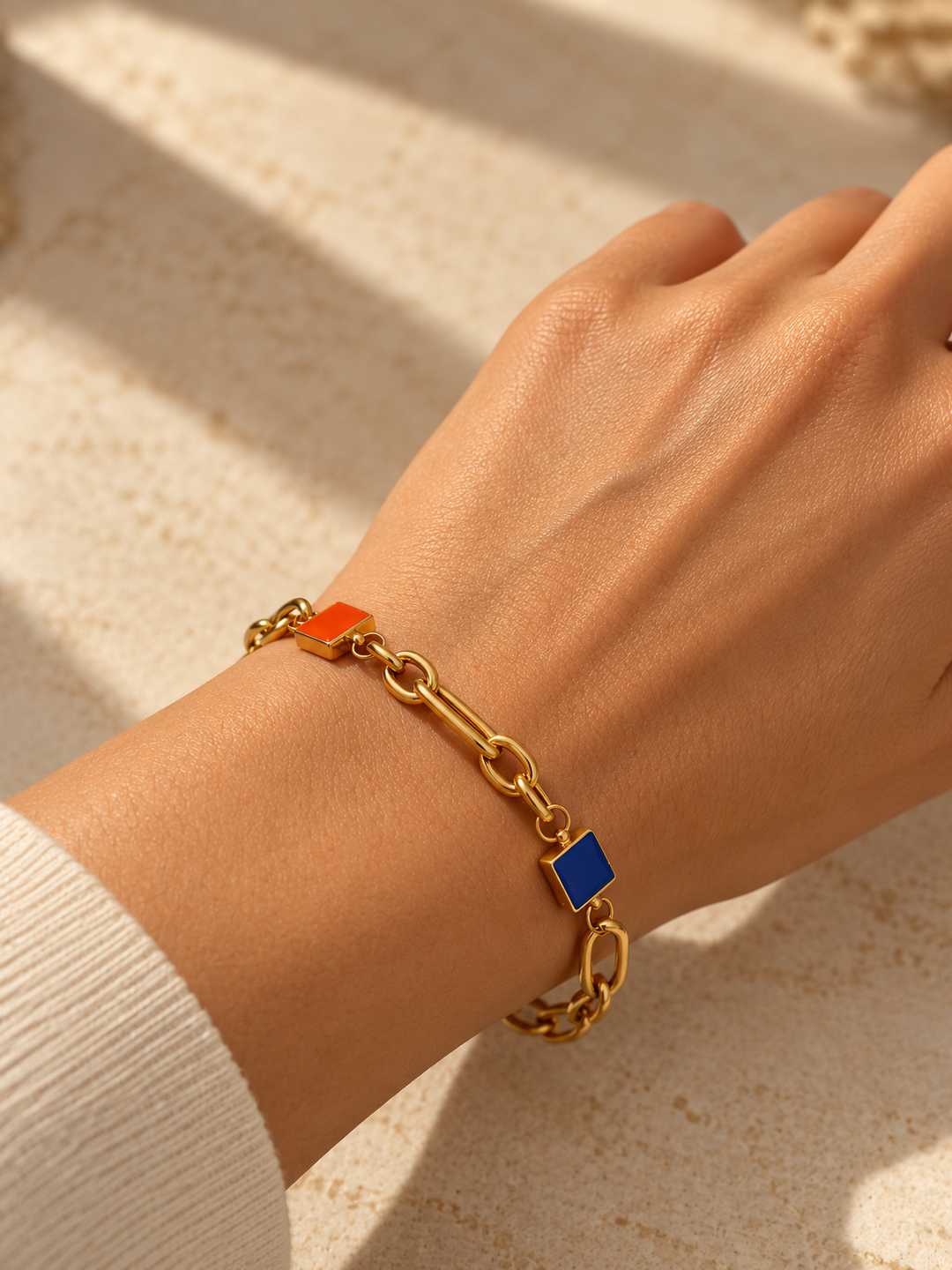 Frau trägt das Armband Rangin aus 18k Gelbgold mit orangefarbenem und blauem Farbakzent am Handgelenk.
