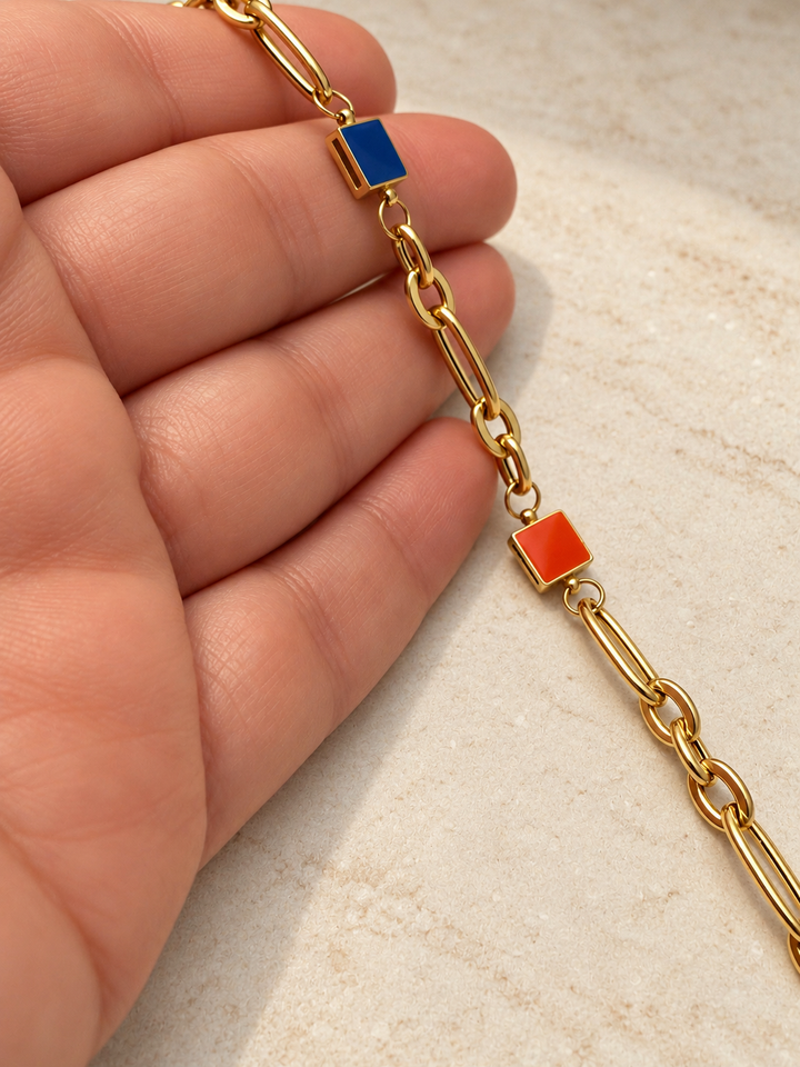 Detailansicht des Armbands Rangin mit orangefarbenem und blauem Quadrat, glänzenden Goldgliedern und geometrischer Gestaltung.