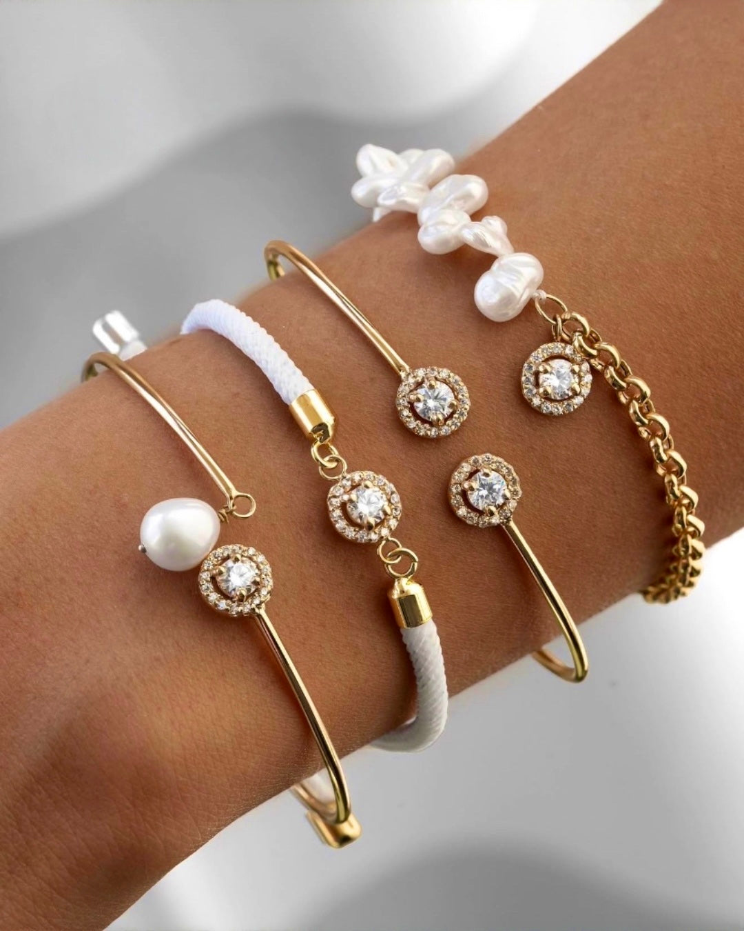 Mehrere Armbänder aus 18 Karat Gelbgold mit Zirkonia, echter Süsswasserperle, weissen Barockperlen und hochwertigem Textilband am Handgelenk. Handgefertigter Luxusschmuck mit modernem Design, der Eleganz, Individualität und zeitlose Schönheit vereint. Ideal für stilbewusste Frauen mit Sinn für besondere Schmuckstücke.