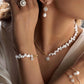 Elegantes Schmuck-Ensemble aus Gelbgold mit weißen Barockzuchtperlen und funkelnden Zirkonia-Steinen. Die Frau trägt eine asymmetrische Perlen-Gold-Halskette mit rundem Anhänger, passende Perlenohrringe, ein Perlenarmband mit Anhänger, einen filigranen Ring mit großem Zirkonia sowie zarte Armreifen mit Perlen- und Zirkonia-Akzenten. Die Kombination aus warmem Gold, strahlenden Steinen und natürlichen Perlen verleiht dem Look zeitlose Eleganz und feminine Raffinesse.