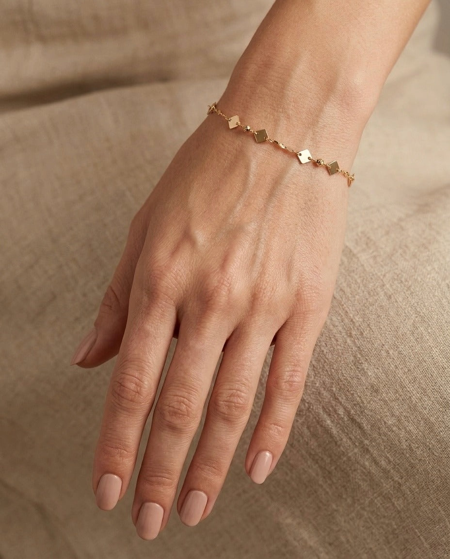 18 Karat Gelbgold-Armband mit quadratischen Goldplättchen und feiner Ankerkette am Handgelenk getragen – minimalistischer, eleganter Damenschmuck von Ziba Gold.