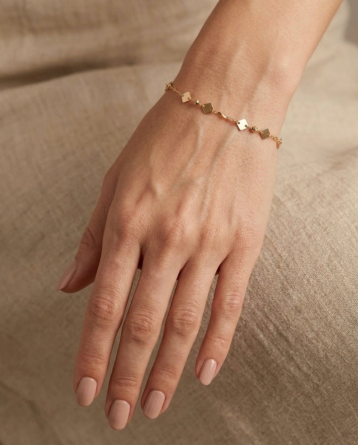 18 Karat Gelbgold-Armband mit quadratischen Goldplättchen und feiner Ankerkette am Handgelenk getragen – minimalistischer, eleganter Damenschmuck von Ziba Gold.