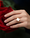 Eleganter 18k Gelbgold-Ring mit Kleeblatt-Motiv aus weißem Perlmutt, getragen an einer Hand vor einer roten Rose; luxuriöser, zeitloser Schmuck mit filigraner Goldfassung und natürlicher Steinstruktur.
