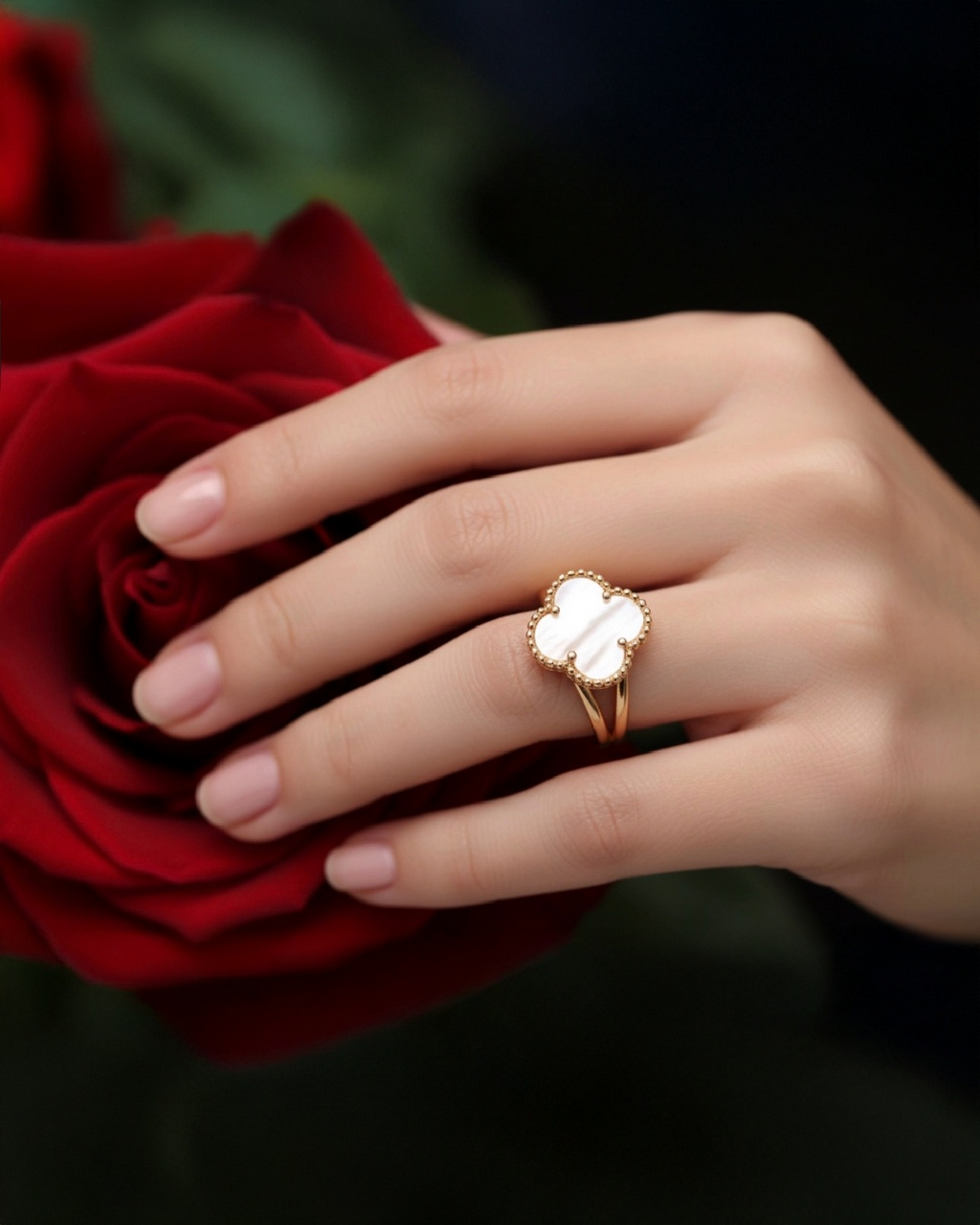 Eleganter 18k Gelbgold-Ring mit Kleeblatt-Motiv aus weißem Perlmutt, getragen an einer Hand vor einer roten Rose; luxuriöser, zeitloser Schmuck mit filigraner Goldfassung und natürlicher Steinstruktur.
