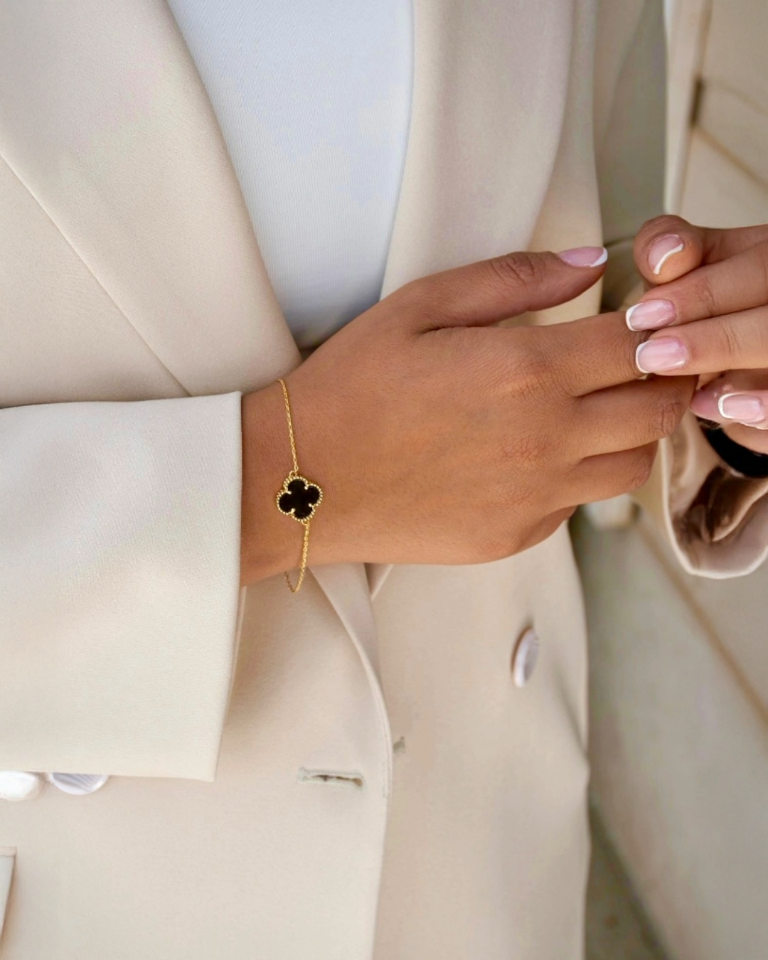 Zweifarbiges Kleeblatt-Armband Shabdar-e Do Rang aus 18k Gelbgold mit schwarzem Inlay – getragen am Handgelenk zu hellem Blazer