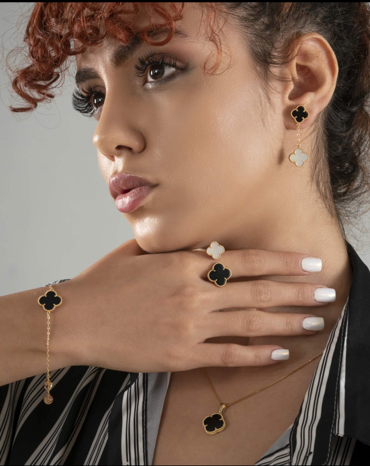 Nahaufnahme eines zweifarbigen Armbands aus 18k Gelbgold mit kleeblattförmigem Anhänger in Schwarz, getragen an einem weiblichen Handgelenk, kombiniert mit passendem Ring, Ohrringen und Halskette.