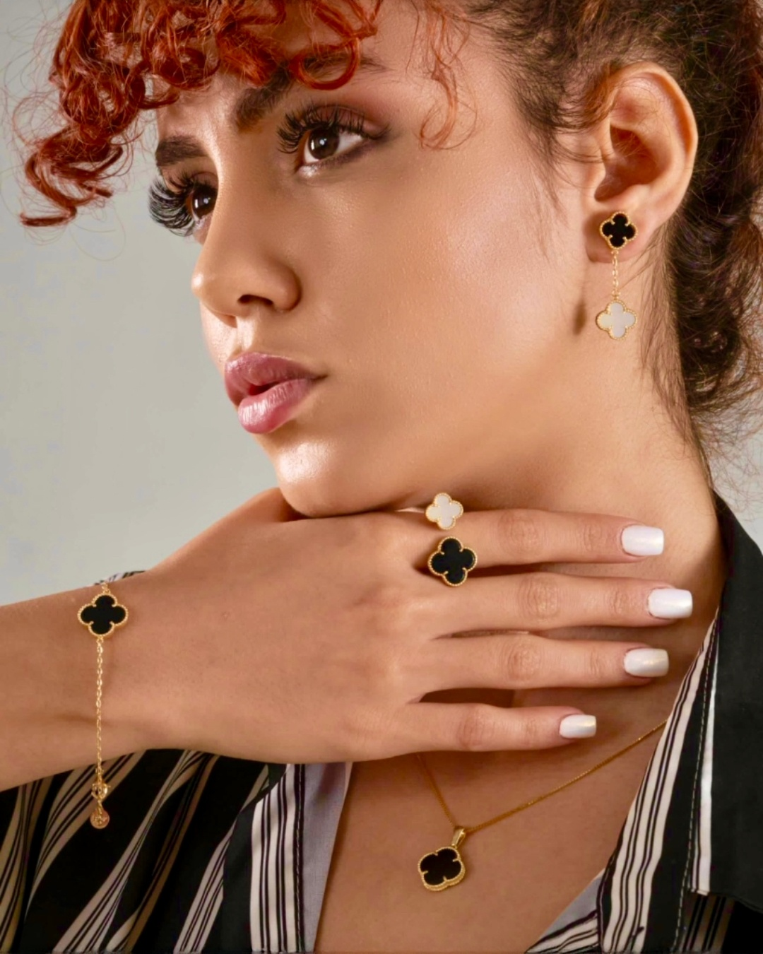 Nahaufnahme eines zweifarbigen Armbands aus 18k Gelbgold mit kleeblattförmigem Anhänger in Schwarz, getragen an einem weiblichen Handgelenk, kombiniert mit passendem Ring, Ohrringen und Halskette.