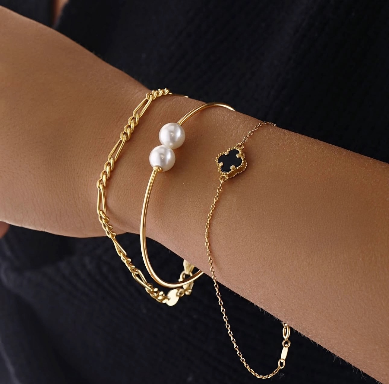 Filigranes 18k Gelbgold-Armband mit kleinem zweifarbigem Kleeblatt-Anhänger in Schwarz und Gold, elegant am Handgelenk getragen.