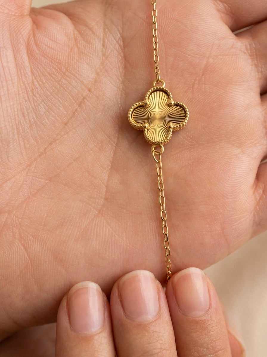 Detailaufnahme eines filigranen Armbands aus 18 Karat Gelbgold mit fein strukturiertem Kleeblatt-Motiv und Goldkügelchen-Bordüre.