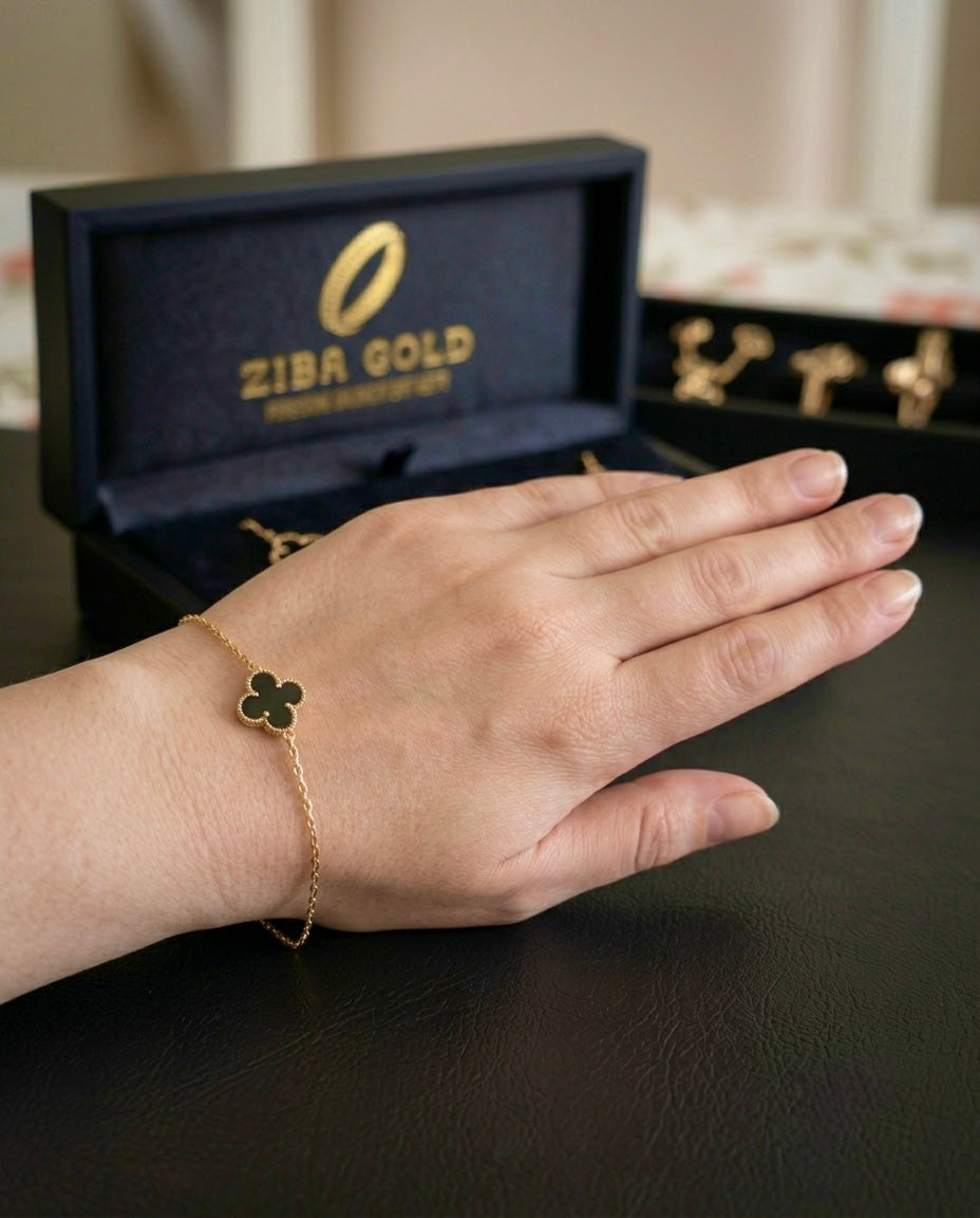 Filigranes Armband aus 18 Karat Gelbgold mit schwarzem Onyx-Kleeblatt am Handgelenk, vor einer Ziba Gold Schmuckbox.
