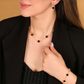 Frau trägt ein elegantes Schmuckset aus 18 Karat Gelbgold mit schwarzen Kleeblatt-Elementen – bestehend aus Halskette, Armband und Ohrringen. Der Look ist edel und modern, kombiniert mit einem schwarzen Outfit.