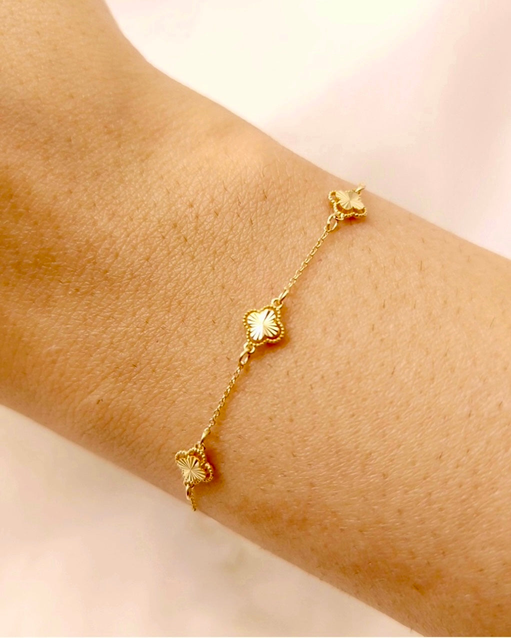 Feines Armband aus 18 Karat Gelbgold mit zarter Kette und drei goldenen Kleeblatt-Elementen, elegant am Handgelenk getragen – ein zeitloses, feminines Schmuckstück.