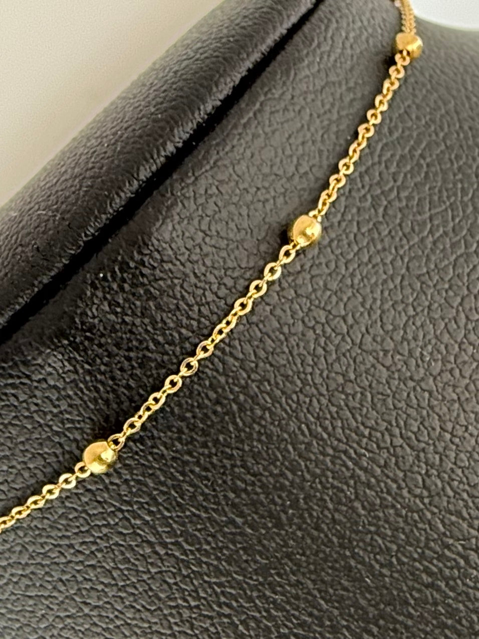 Nahaufnahme auf schwarzer Büste: zartes Goldarmband mit Akzenten.