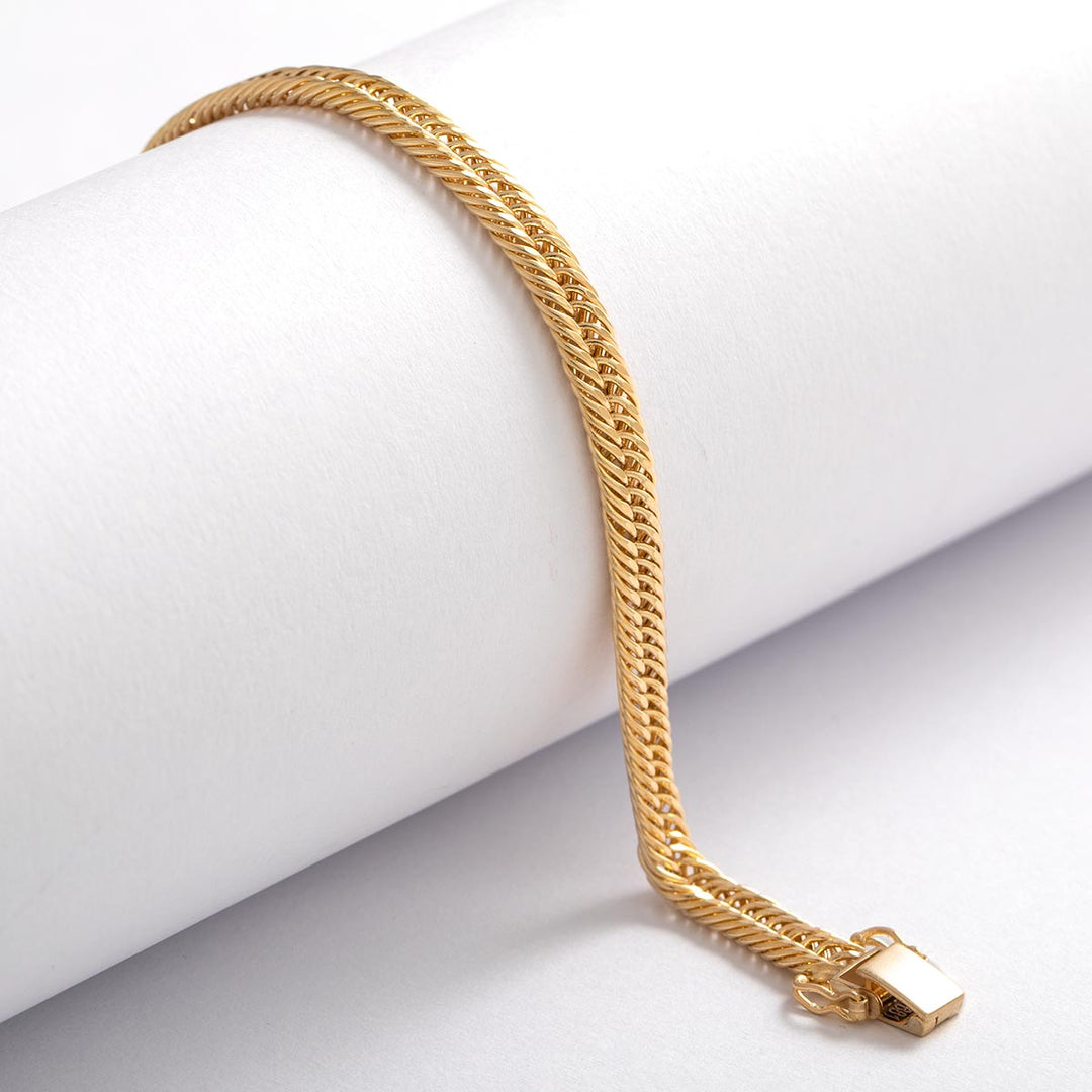 Armband aus 18 Karat Gelbgold mit fein gewebter, flach anliegender Struktur und polierter Oberfläche, dekorativ um eine weiße Rolle drapiert, mit rechteckigem Sicherheitsverschluss.
