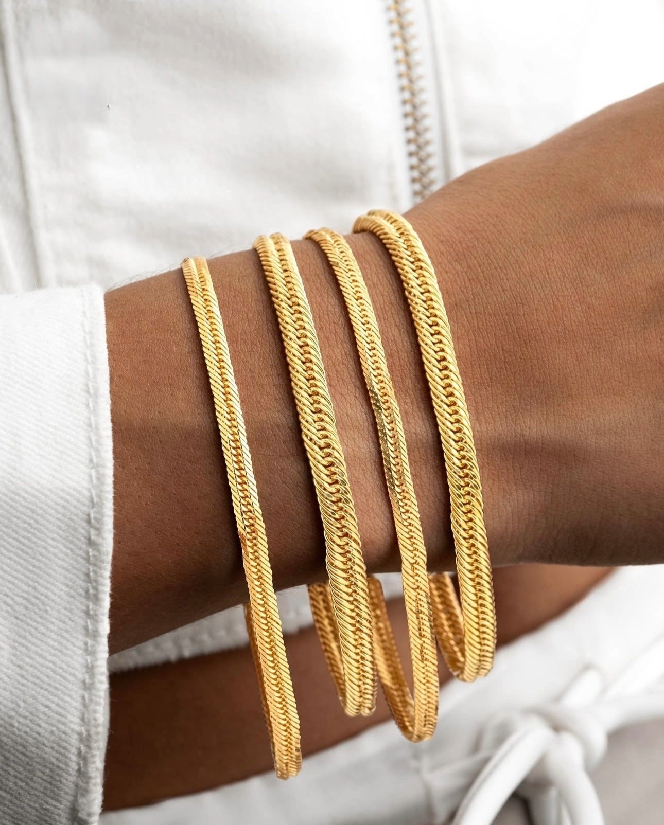 Vier Armbänder aus 18 Karat Gelbgold im gewebten Design „Talā-ye Tanideh“, eng aneinander am Handgelenk getragen – luxuriös, glänzend und handgefertigt mit eleganter Struktur.