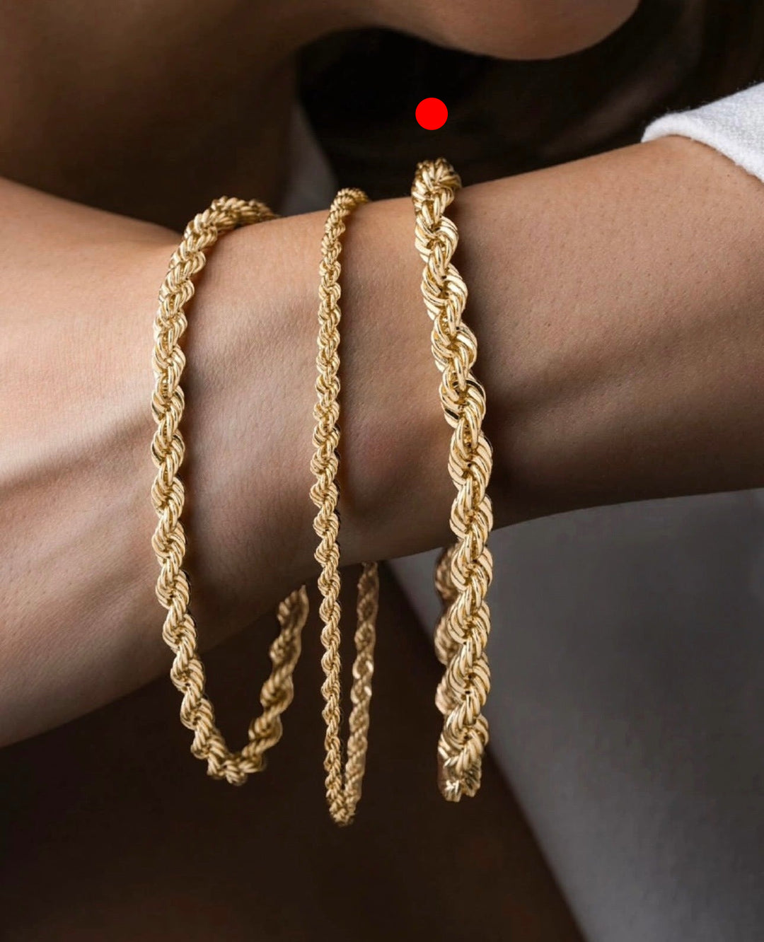 Mehrere Armbänder aus 18k Gelbgold in Kordel- und Ringzopfstruktur, handgefertigt und übereinander am Handgelenk getragen, warmes Gold auf natürlicher Haut.