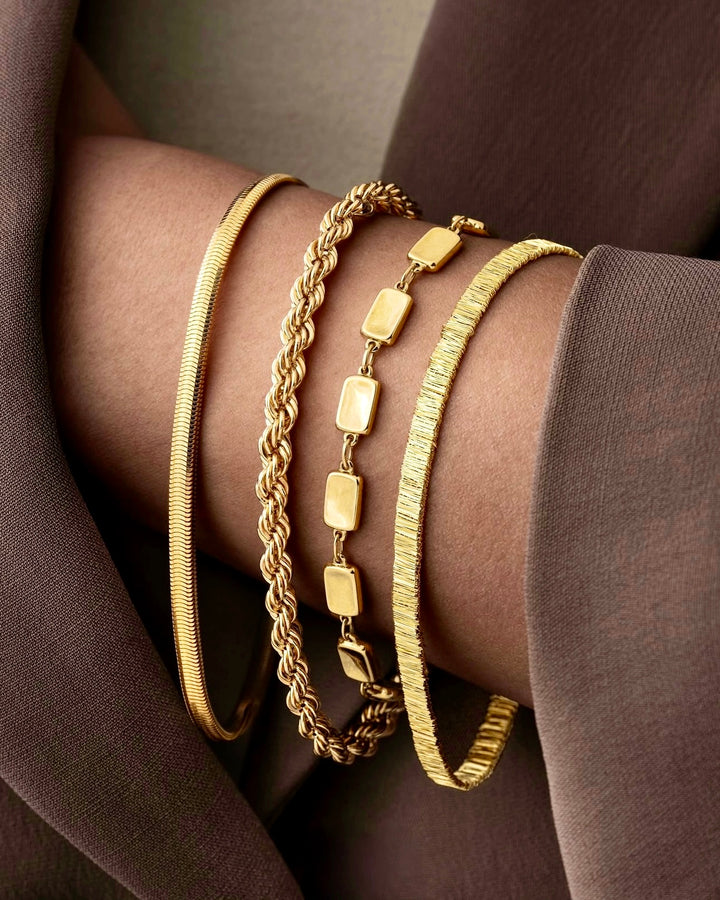 Vier handgefertigte Armbänder aus 18k Gelbgold im Mix aus Zopf-, Glieder- und Bangle-Design – kombiniert am Handgelenk für eleganten Layering-Look