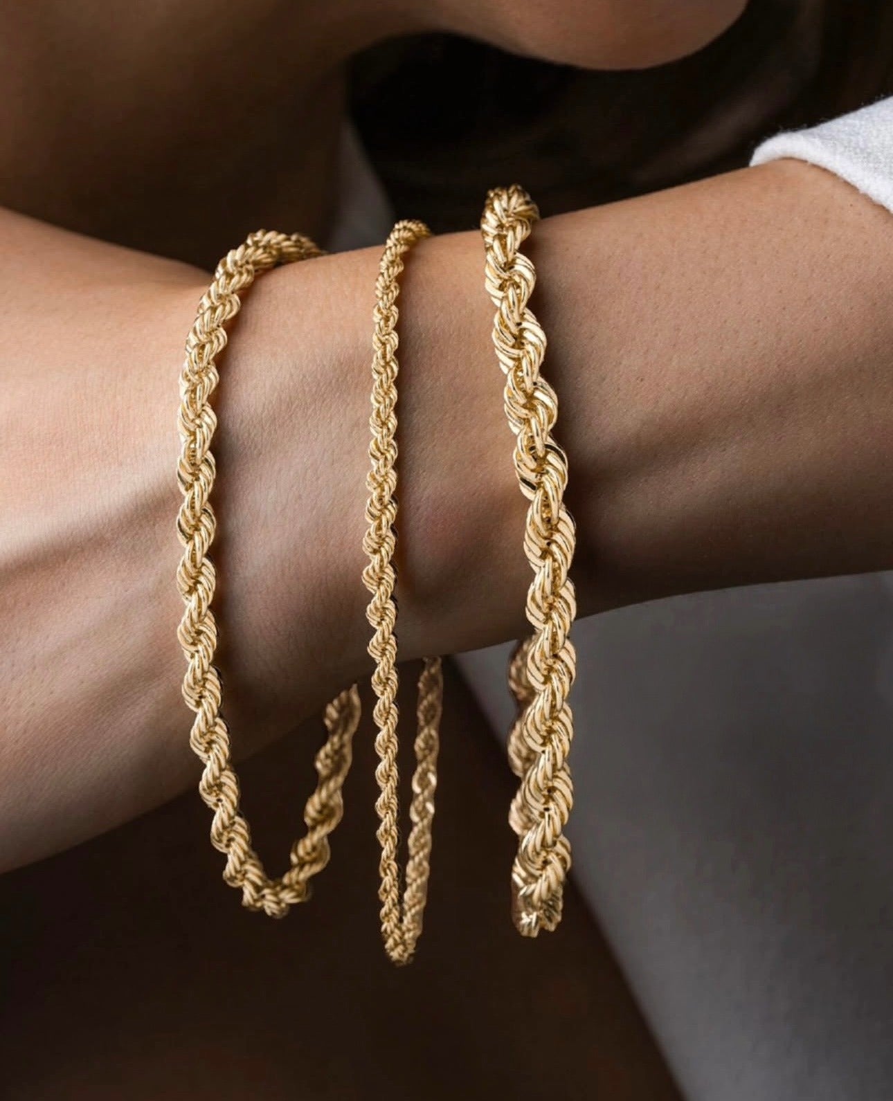 Nahaufnahme eines eleganten Armbands aus 18k Gelbgold – Tanab-e Tala (Goldene Kordel) – mit kunstvoll gedrehter Kordelstruktur, das stilvoll um das Handgelenk einer Person gelegt ist.