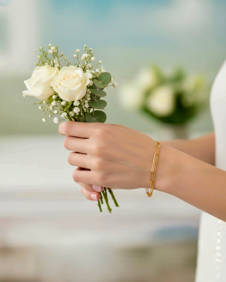 Elegantes Damenarmband aus 18k Gelbgold am Handgelenk, getragen von einer Frau mit weißem Rosenstrauß – zeitloser Goldschmuck, feminin, edel und stilvoll.