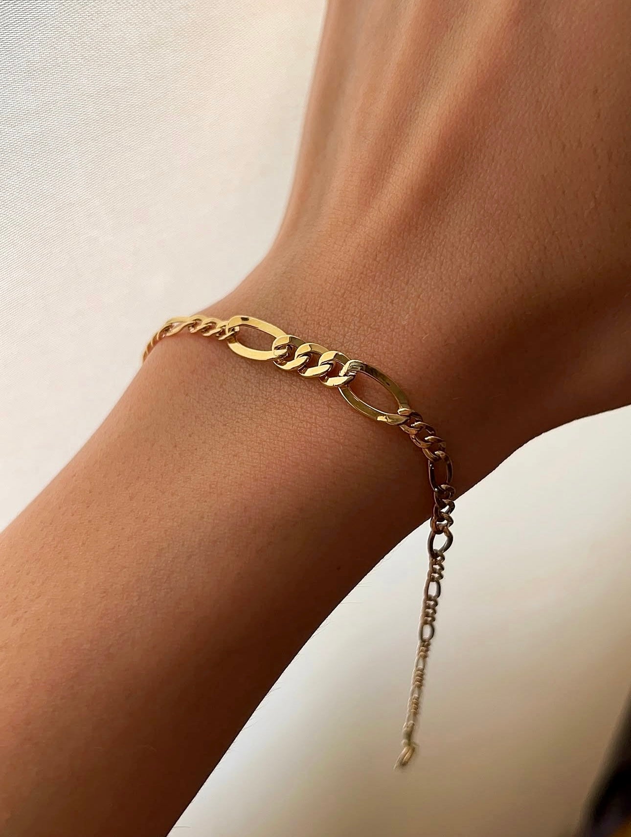 Nahaufnahme eines eleganten Figaro-Armbands aus 18 Karat Gelbgold am Handgelenk, mit abwechselnd langen und kurzen Kettengliedern in konischer Form und feiner Verlängerungskette.