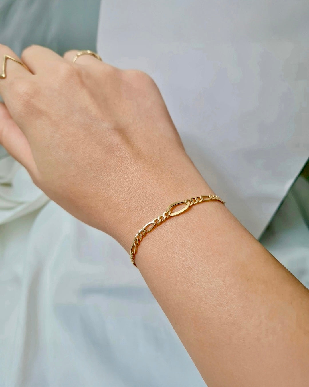 Feines 18k Gelbgold-Armband im Figaro-Stil am Handgelenk, mit einem markanten ovalen Mittelglied und zarten, polierten Kettengliedern.