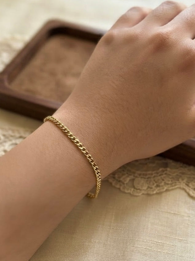 Nahaufnahme eines filigranen goldenen Panzerarmbands am Handgelenk einer Frau, elegant und dezent getragen vor einem warmen, natürlichen Hintergrund.