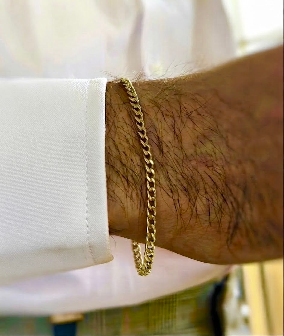 Nahaufnahme eines feinen goldenen Panzerarmbands am Handgelenk eines Mannes, kombiniert mit einem weissen Hemd und elegant getragen.