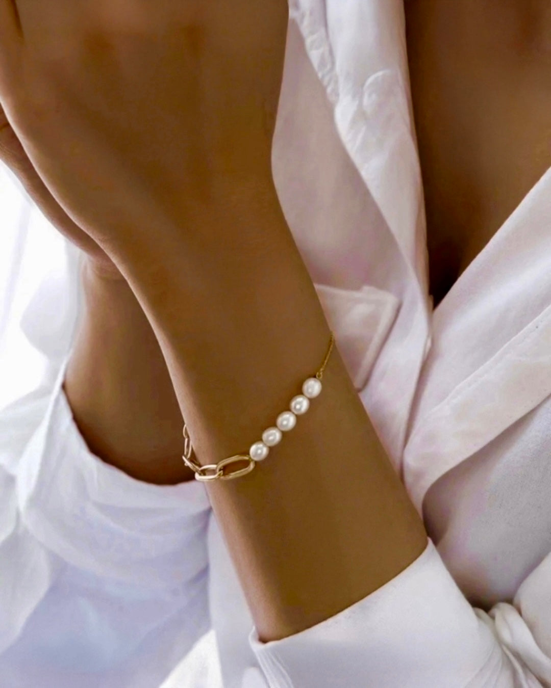 Armband aus 18k Gelbgold mit feinen Gliedern und fünf weißen Perlen, getragen am Handgelenk einer Frau vor hellem Stoffhintergrund.