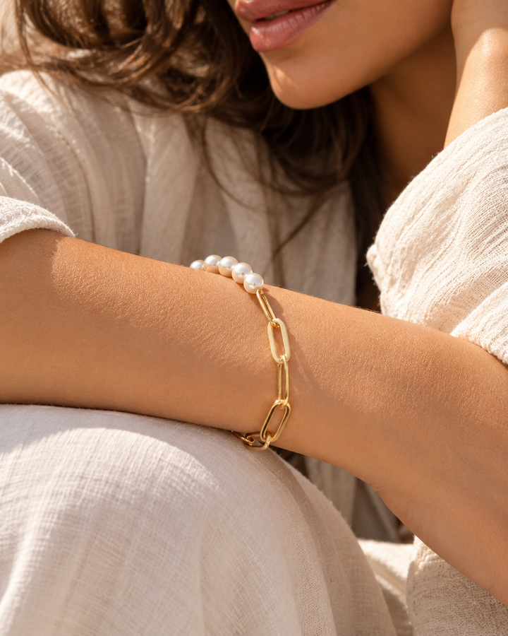 Elegantes Armband mit schimmernden Perlen und länglichen Gliedern aus Gelbgold am Handgelenk einer Frau, stilvoll inszeniert in warmem, natürlichem Licht.