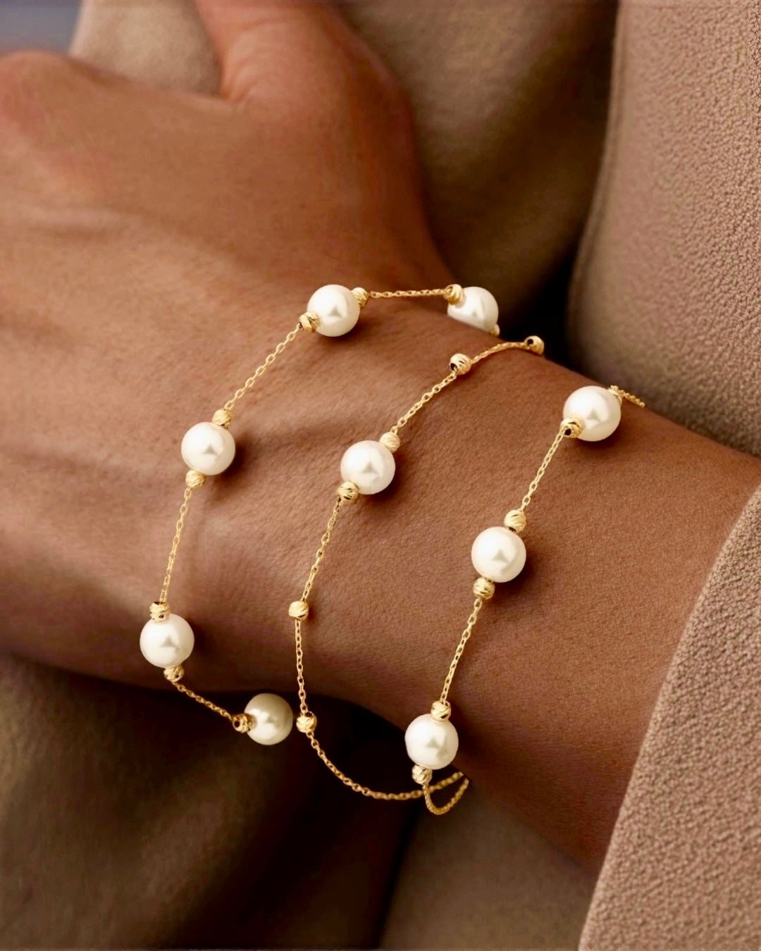 18k Gelbgold Armband mit feiner Ankerkette, gleichmäßig verteilten Goldkugeln und echten weißen Perlen, elegant am Handgelenk getragen, filigranes Design in warmem Licht.