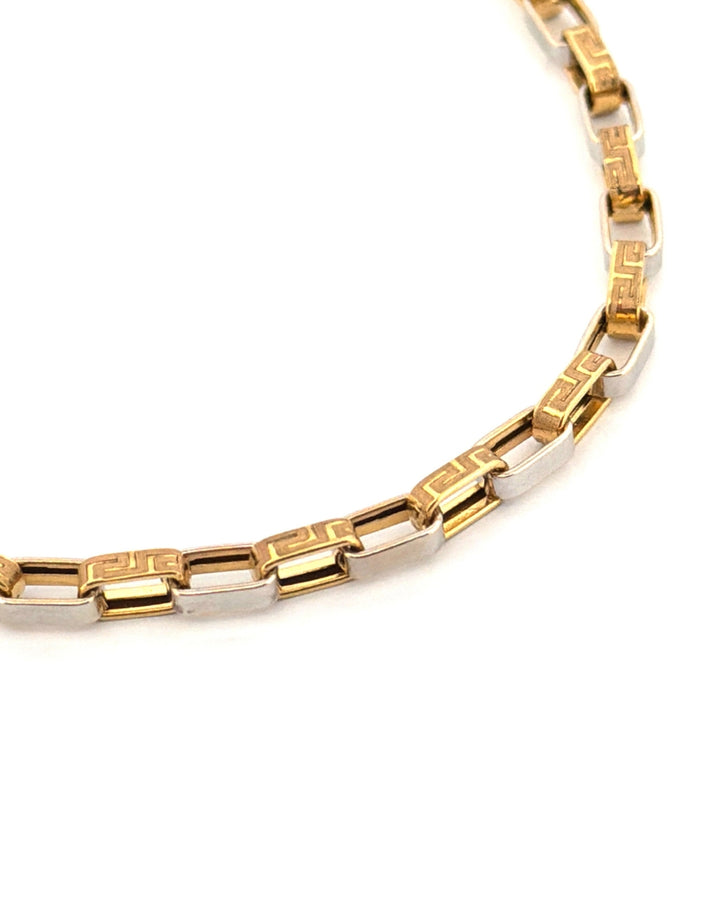 Detailaufnahme eines 18-karätigen Bicolor-Armbands aus Gelb- und Weissgold. Die rechteckigen Gelbgold-Elemente sind mit einem fein gravierten, geometrischen Mäandermuster verziert und werden durch polierte Weissgold-Glieder miteinander verbunden. Die Nahaufnahme hebt die präzise Verarbeitung, die glänzenden Oberflächen und das moderne, elegante Design des Schmuckstücks vor hellem Hintergrund hervor.