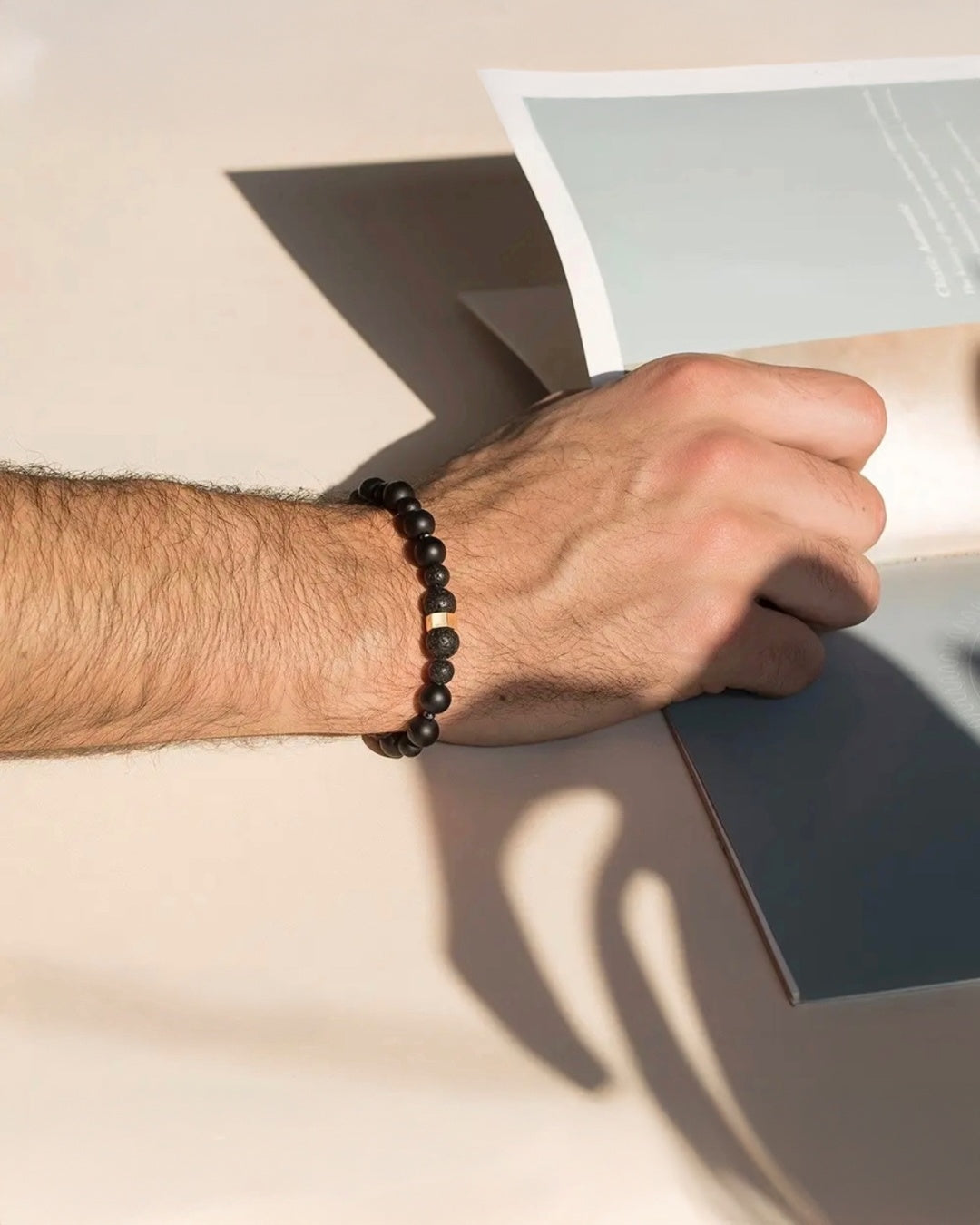 Armband aus Vulkanstein- und Onyxkugeln mit einem Hexagon aus 18k Gold – getragen am männlichen Handgelenk, natürlich & kraftvoll