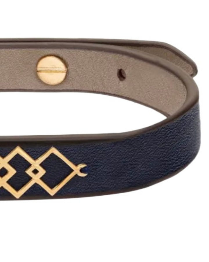 Detailaufnahme eines dunkelblauen Lederarmbands mit goldfarbenem geometrischem Ornament, innen helles Lederfutter, sichtbare Schraubniete und Lochung für den Verschluss.