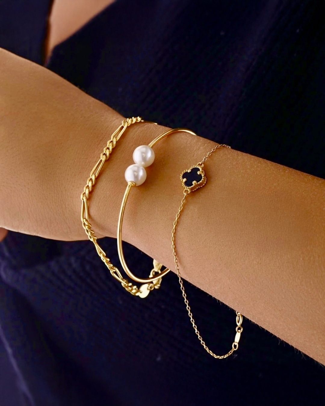 Filigranes 18k Gelbgold-Armband mit kleinem zweifarbigem Kleeblatt-Anhänger in Schwarz und Gold, elegant am Handgelenk getragen.