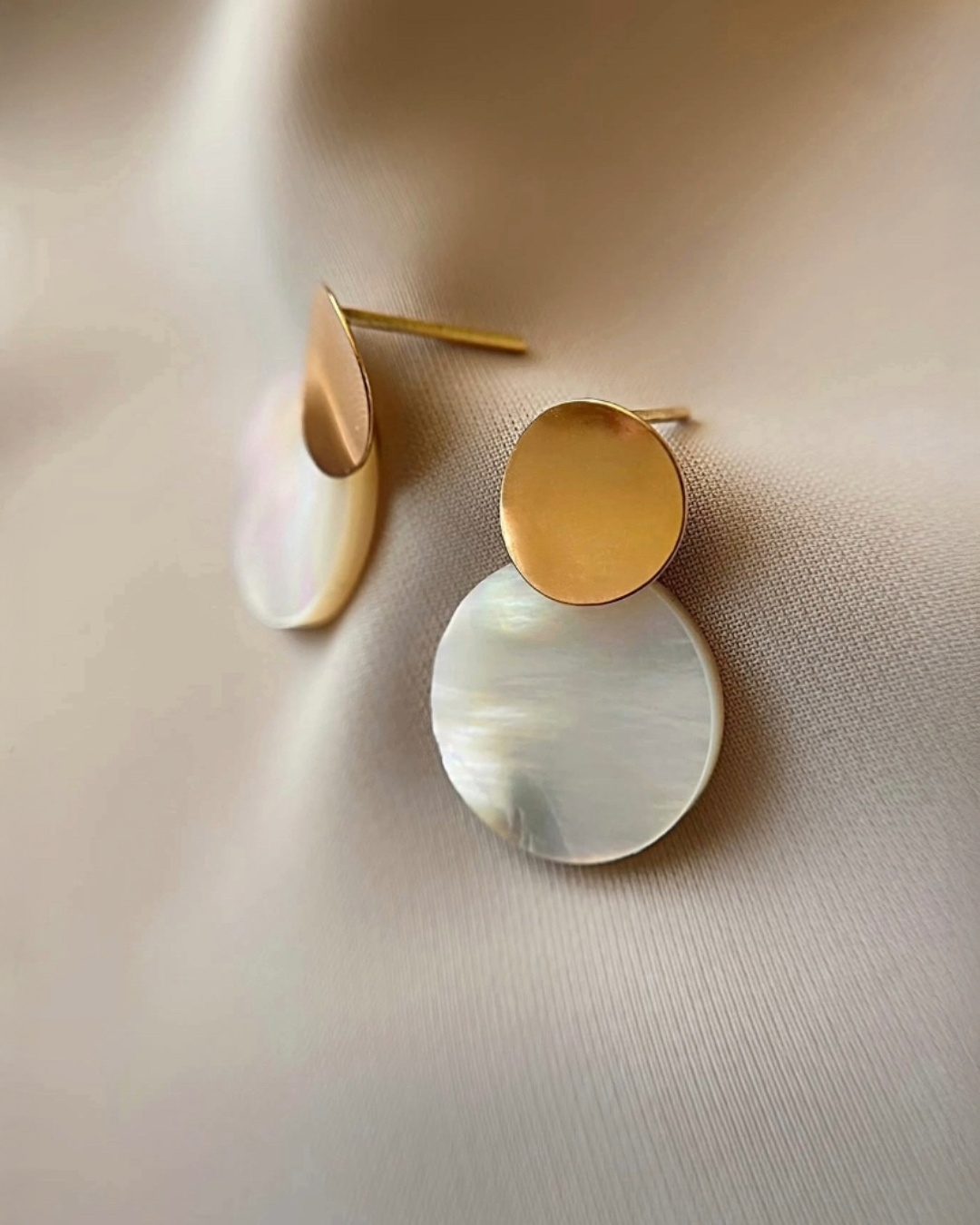 Detailaufnahme von Perlmutt-Ohrringen aus 18k Gelbgold, runde Scheibenform mit matter Goldoberfläche, eleganter minimalistischer Damenschmuck