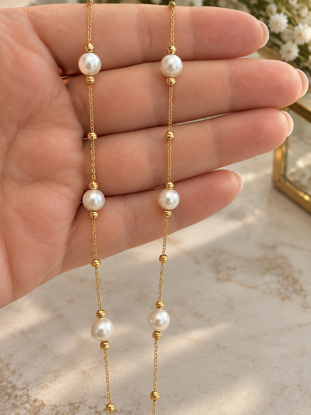 Detailaufnahme der filigranen 18K Goldhalskette mit weissen synthetischen Perlen und kleinen Goldkügelchen auf einer Hand.