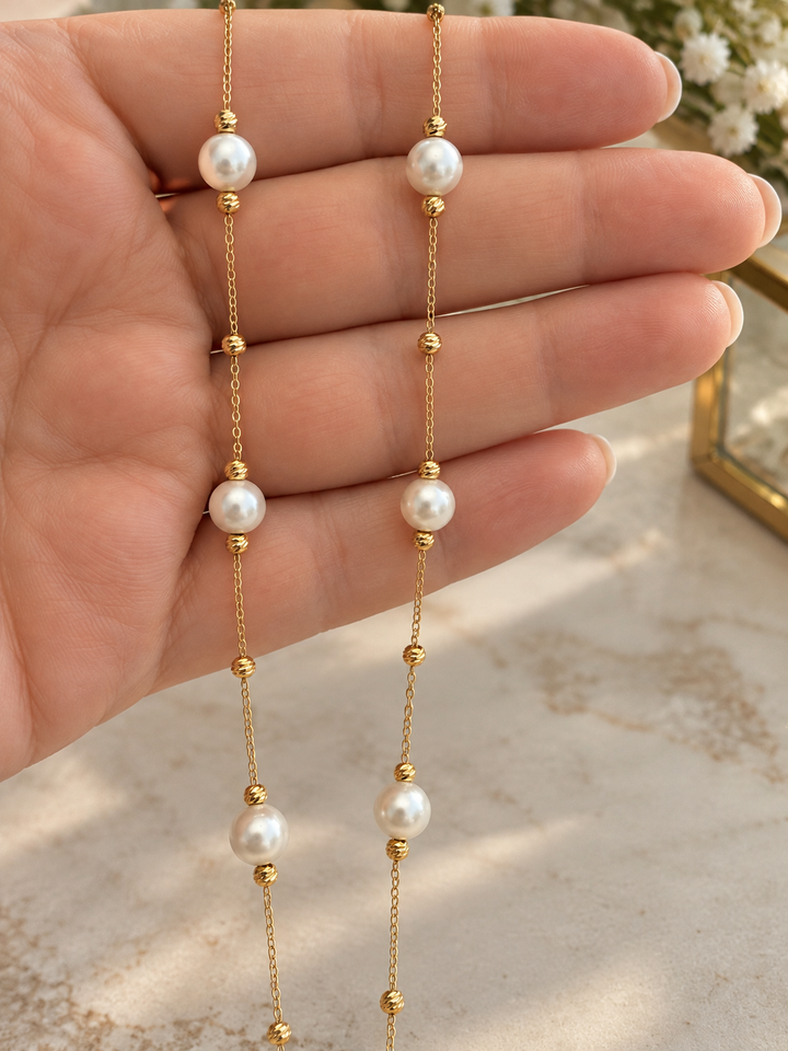 Detailaufnahme der filigranen 18K Goldhalskette mit weissen synthetischen Perlen und kleinen Goldkügelchen auf einer Hand.
