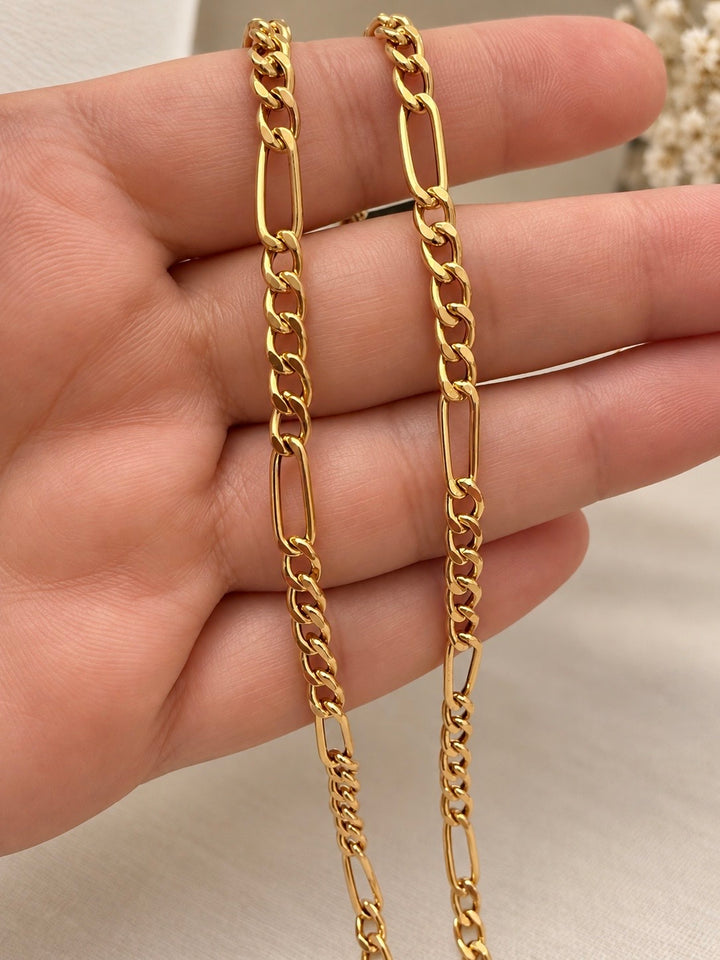 Nahaufnahme der 4 mm breiten Figaro-Goldkette mit polierten Panzerkettengliedern und länglichen offenen Gliedern auf einer Hand.