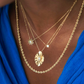 Mehrlagige Halsketten aus 18 Karat Gelbgold – kombiniert aus einer gedrehten Kordelkette und feinen Ketten mit Anhängern, darunter eine Sonne mit Zirkonia, ein runder Stein und ein kunstvoll gearbeiteter Anhänger, getragen zu einem blauen Oberteil.