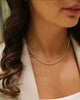 Nahaufnahme einer Frau mit lockigem, braunem Haar, die eine elegante Halskette aus 18k Gelbgold mit feiner, gedrehter Gliederstruktur trägt. Sie trägt ein helles Oberteil und ein cremefarbenes Blazer-Jackett, aufgenommen bei weichem, natürlichem Licht.