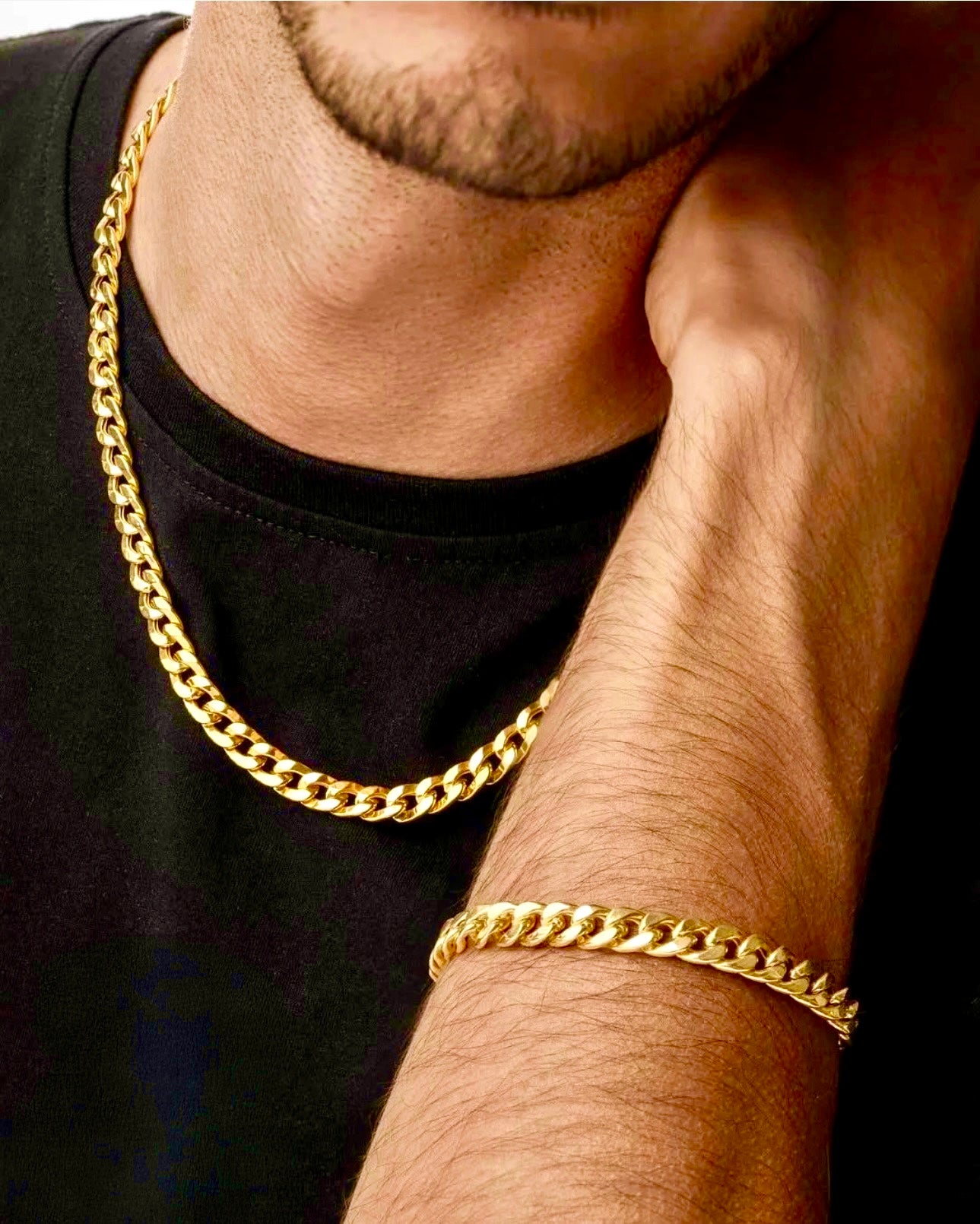 Nahaufnahme eines Mannes in schwarzem Shirt, der eine Halskette aus 18k Gelbgold trägt – Zanjir-e Shah (Königliche Kette), mit passendem Armband im gleichen massiven Kettendesign.